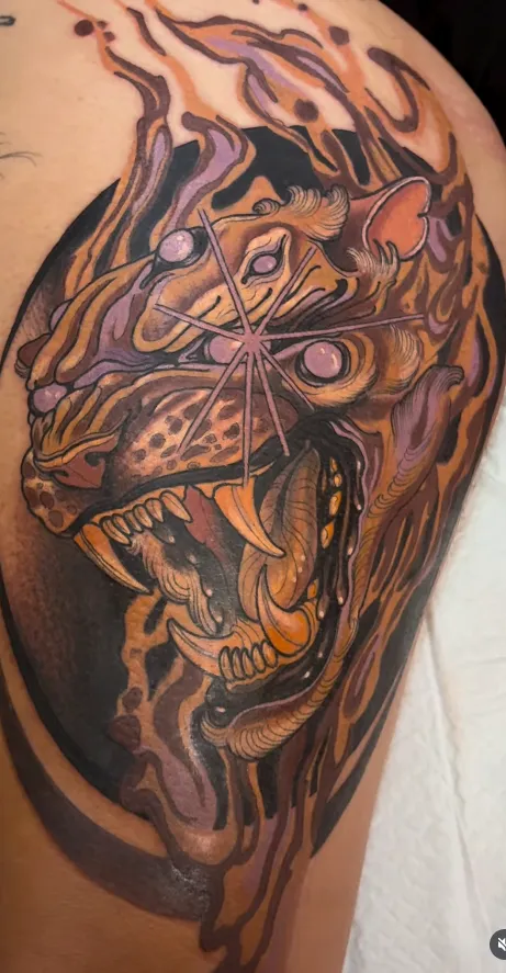 Snarling beast tattoo on the thigh rendered in purple, amber and black neo-traditional colour.