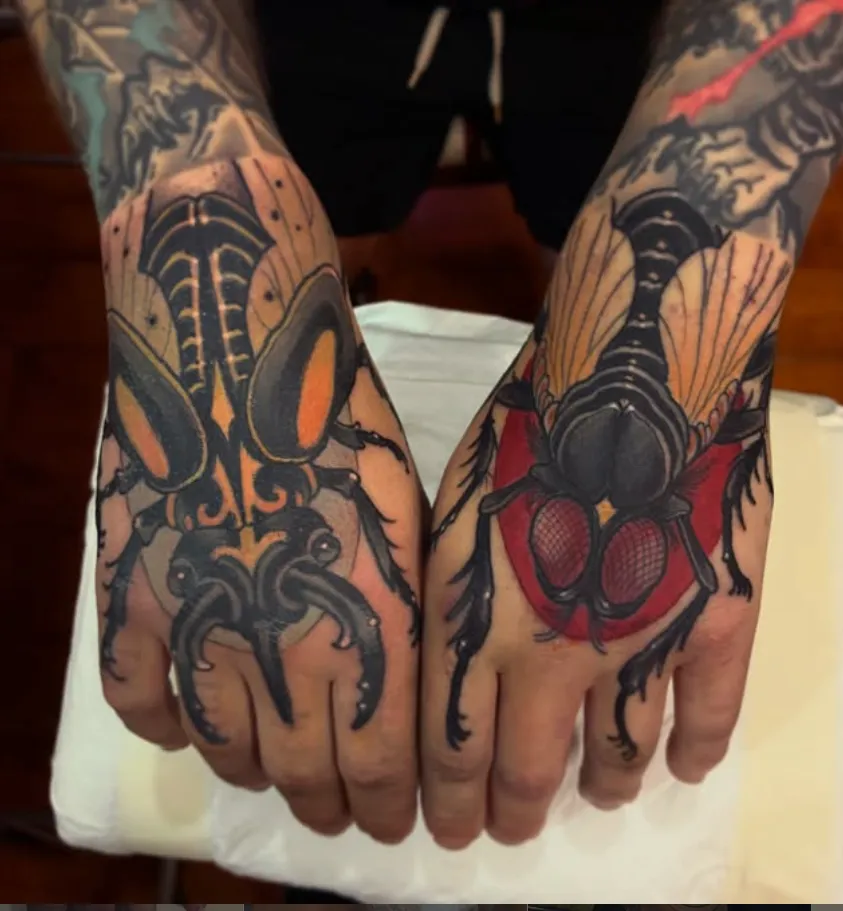 Matching beetle tattoos across the backs of both hands in bold black, amber and red neo-traditional colour.